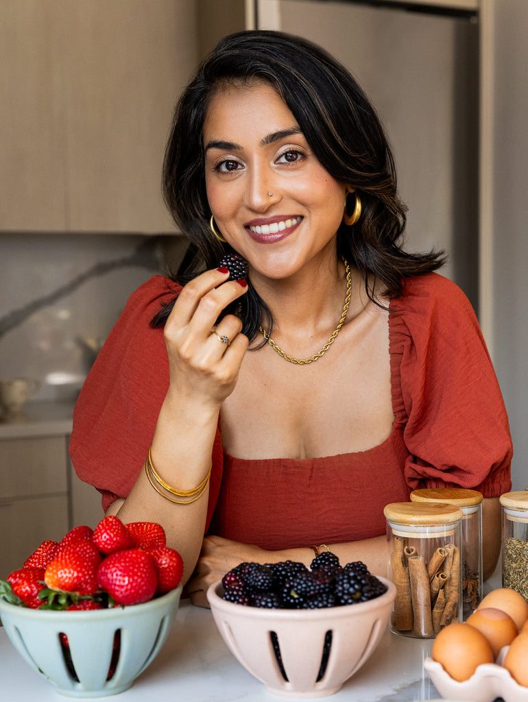 Woman holding a blackberry in a kitchen setting with jars and fruits.